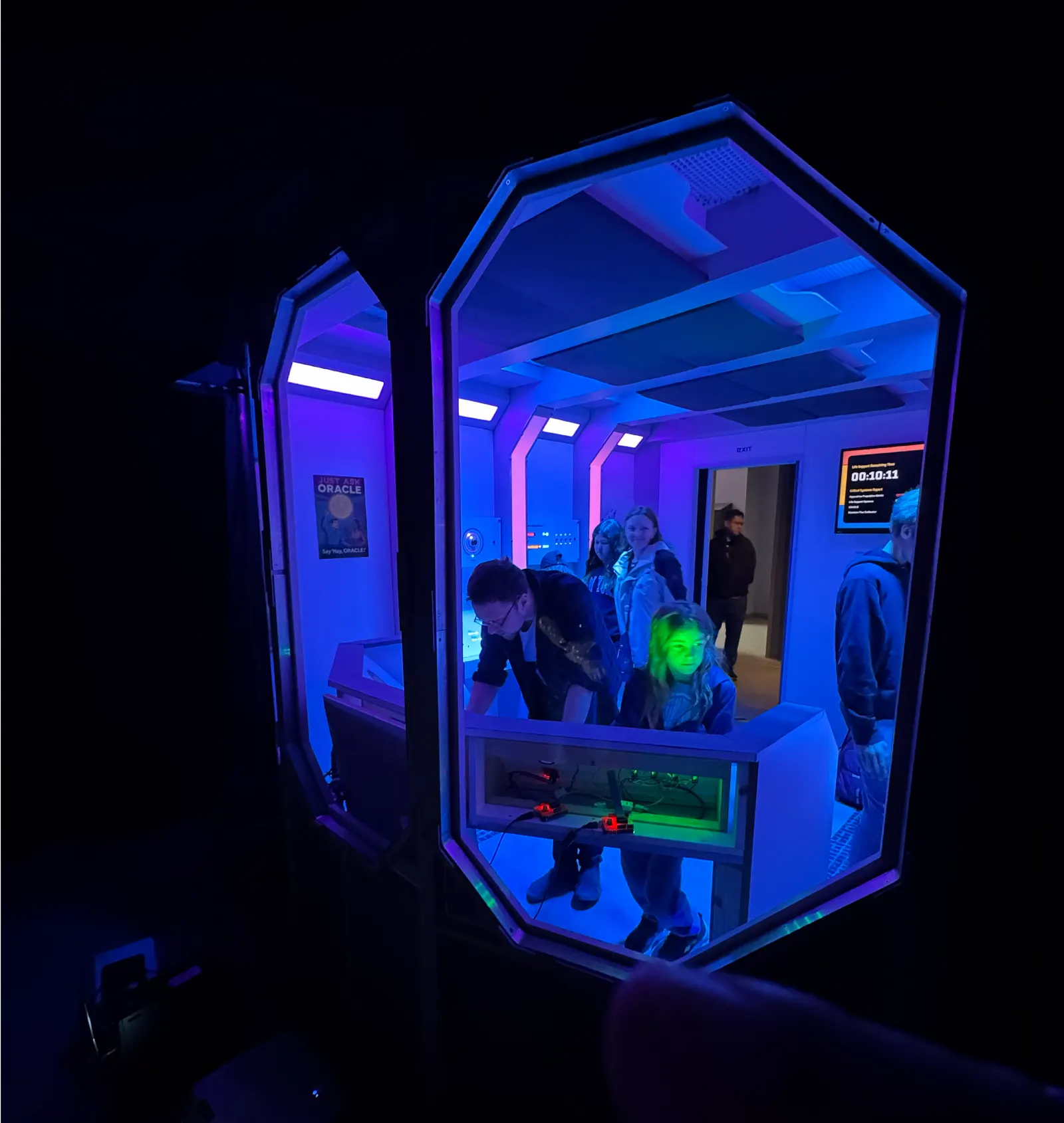 Spaceship-themed escape-room interior with blue and purple lighting, control consoles, and a countdown timer, seen through an octagonal portal