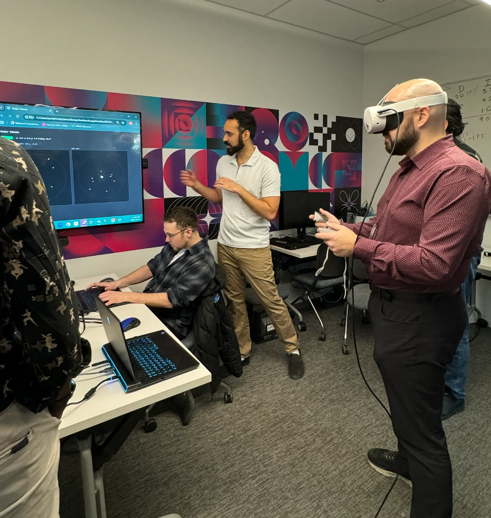 A participant wears a Meta Quest headset during a playtest while developers monitor the session and review radar-style telemetry on a wall-mounted display